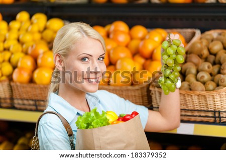 Choosing grape girl hands bag with fresh vegetables against the shelves of fruits in the store