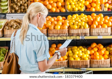 Girl looks through shopping list near the pile of fruits lying in the braided baskets in the store