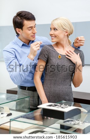 Young man puts necklace on his girlfriend at jeweler\'s shop. Concept of wealth and luxurious life