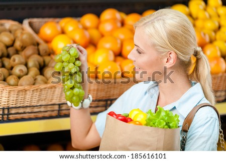 Choosing grape girl hands bag with fresh vegetables against the shelves of fruits in the market