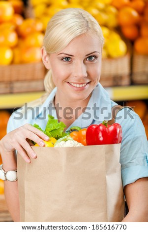 Girl hands paper bag with fresh vegetables against the shelves of fruits in the shop