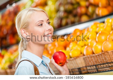 Girl at the store choosing fruits and vegetables hands fresh red apple