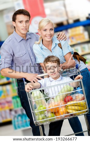Family drives cart with food and son sitting there. Concept of fresh and healthy food and consumerism