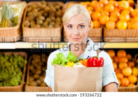 Girl hands bag with fresh vegetables against the shelves of fruits in the shop