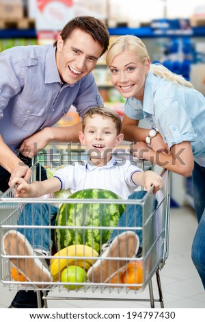 Family drives cart with food and boy sitting there with watermelon. Concept of fresh and healthy food and consumerism