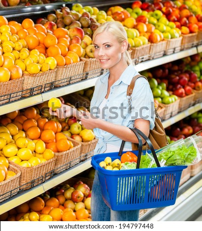 Girl at the shop choosing fruits and vegetables hands lemon and full of purchases hand cart