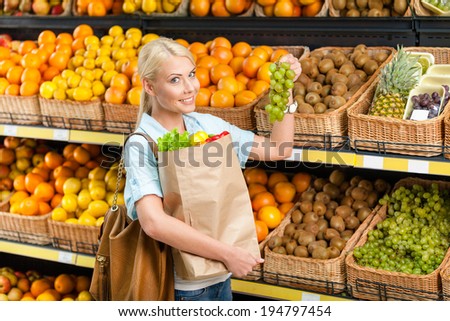 Choosing grape girl hands bag with fresh vegetables against the shelves of fruits in the shop
