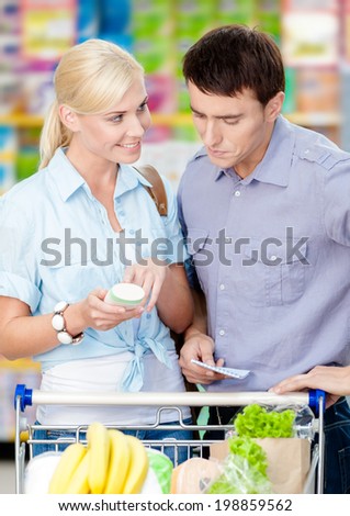 Couple discussing the shopping list and chosen products standing near the cart full of food