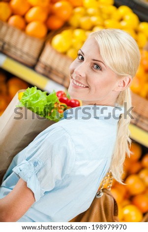Girl hands paper bag with fresh vegetables against the shelves of fruits in the store
