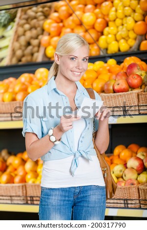 Girl looks through shopping list near the heap of fruits lying in the braided baskets in the store