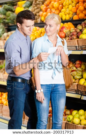 Young couple with shopping list against the piles of fruits decides what to buy
