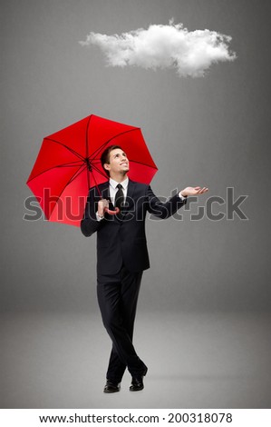 Palming up man with opened umbrella checks the rain and looks at the cloud overhead, isolated on grey