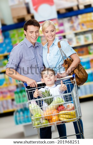 Family drives cart with food and boy sitting there. Concept of fresh and healthy food and consumerism