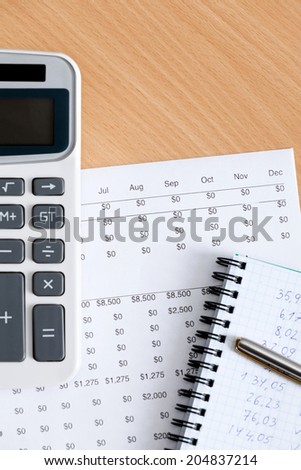 Close up of business stationery: writing pad, pen, calculator and some documents lying on the table