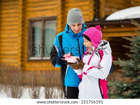 Half-length portrait of man giving present to woman outdoors during winter vacations