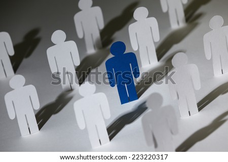 Close up of group of standing paper dolls. Lots of similar copies of a paper man, but a blue one stands out among them. Concept of teamwork and leadership