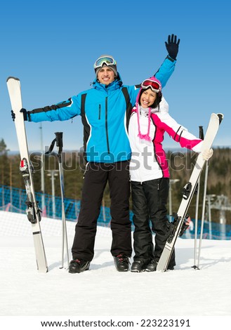Full-length portrait of two hugging skiers with skis in hands