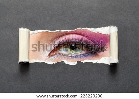 Close up of female eye with pink make-up on torn paper. Concept of fashion and beauty.
