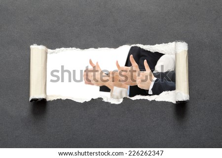 Thumb up businessmen in torn black paper, isolated on black background