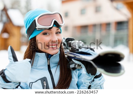 Close up of female wearing sports jacket and goggles who hands skis and thumbs up