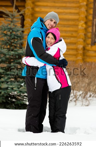 Full-length portrait of embracing couple who wears warm caps and jackets during winter holidays
