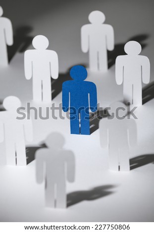 Close up of group of standing paper men. Lots of similar copies of a paper man, but a blue one stands out among them. Concept of teamwork and leadership