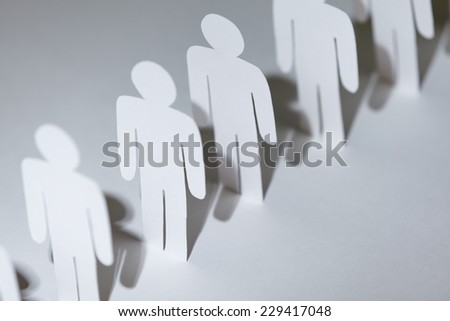 Close up of group of paper-men standing in a row. Lots of copies of one paper man, isolated on white
