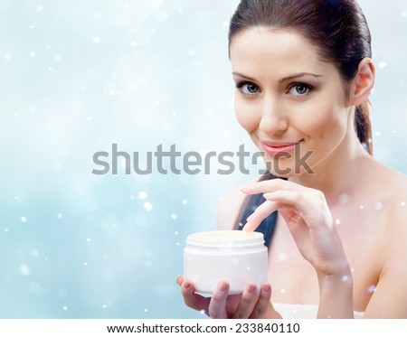 Woman holding emollient cream container and starting to apply moisturizing cream, snow background