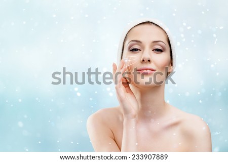 Woman with headband making face moistening procedures in winter time, snowfall background