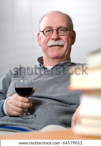 Senior man reading books while sitting on couch with a glass of wine