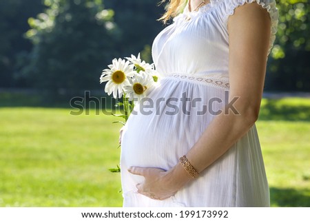 future mother in white dress belly support. closeup. Outdoors, with daisies.