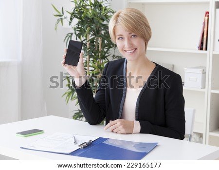 beautiful business woman in the office shows the smartphone screen and smiling