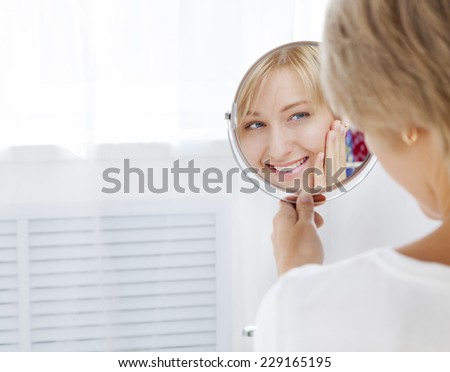 beautiful young woman in the morning, looks in the mirror, touches the face and smiling