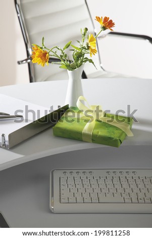 Office scene with flower vase, gift parcel and keyboard on desktop