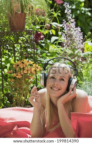 Austria, Woman lying on mattress in garden, listening music