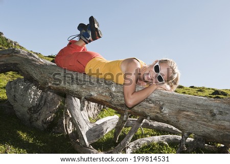 Young woman lying on front on fallen tree trunk, smiling.