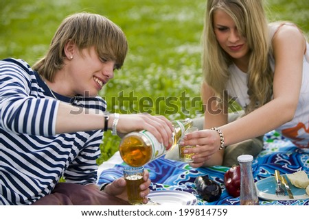Young couple in meadow, boy pouring juice