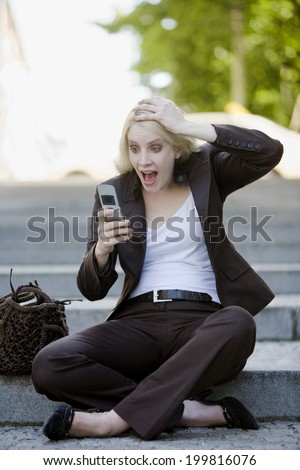 Young woman using mobile phone, sitting on steps, hand to head