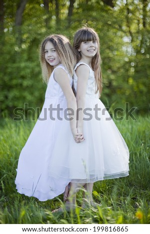 Germany, Bavaria, Two girls (8-9) standing back to back outdoors, smiling,portrait