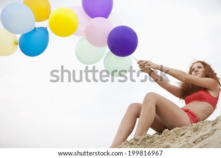 Germany, Bavaria, Young woman on sand dune holding bunch of balloons
