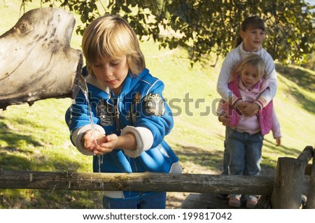 Boy washing hands at fountain, girls standing behind