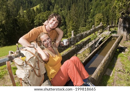 Woman sitting on wooden trough, holding man, smiling.