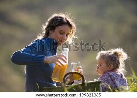 Mother sitting with daughter in meadow, mother pouring juice