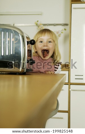 Girl sticking tongue out behind toaster in kitchen