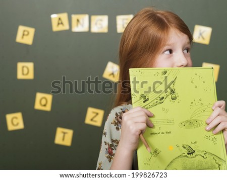 Girl standing by blackboard holding exercise book
