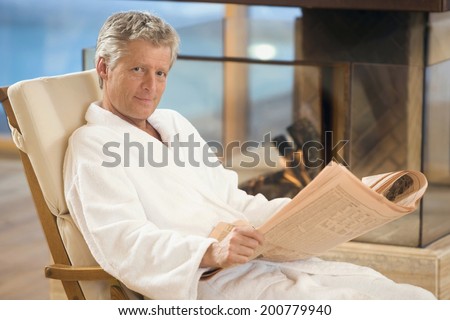 Man in a bathrobe sitting in deckchair holding newspaper smiling