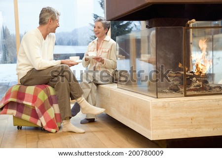 Mature couple sitting in front of fireplace holding tea cup