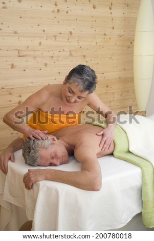 Mature couple man lying on massage table woman stroking man\'s head other hand on man\'s back