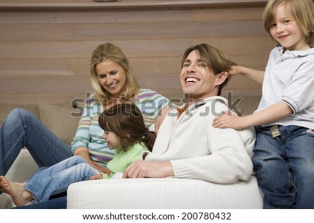 Family sitting together in living room all smiling son pulling father\'s hair