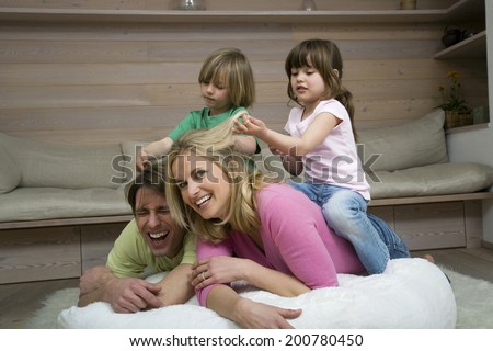 Family in living room children sitting on parent\'s back playing pulling parent\'s hair